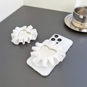 Detail of heart mirror phone grip with white satin ruffle lace on a modern desk