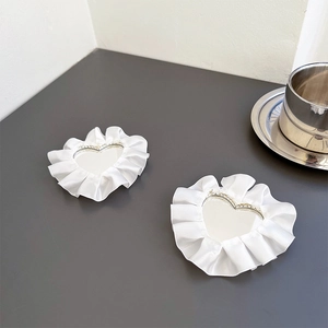 Detail of two heart-shaped makeup mirrors with elegant white lace borders on a grey desk
