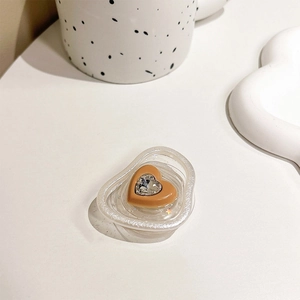 Close-up of heart-shaped acrylic phone grip with central rhinestone on a desk