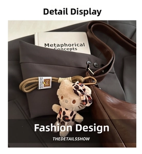 Leopard print plush kitten charm with woven strap and metal clip on a brown tote bag