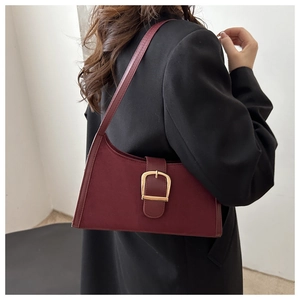 Detail of burgundy suede shoulder bag with a gold buckle worn by a model in a black suit