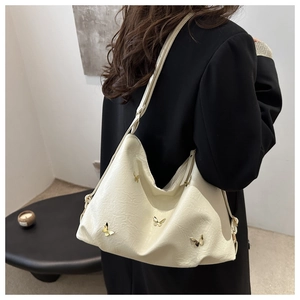 Close-up of cream pleated shoulder bag with gold butterfly accent on a model's arm