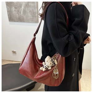 Close-up of a burgundy glossy PU leather hobo bag featuring a cute plush kitten charm