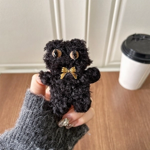 Close-up of black plush bear phone grip with golden NICE bow tie on a wooden table