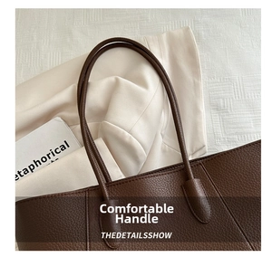 Detail of dark brown pebbled leather tote bag with sturdy handles on a neutral backdrop