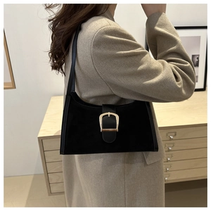 Detail view of black suede underarm bag with gold buckle on a model in a minimal setting