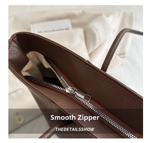 Detailed close-up of smooth silver metal zipper on a brown pebbled leather tote bag