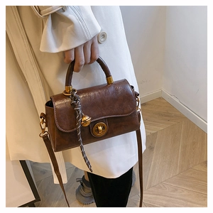 Dettaglio borsa vintage in pelle marrone con chiusura a rotazione dorata e corda intrecciata