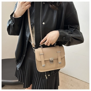 Detail of beige minimalist crossbody bag with silver buckle worn over black leather jacket