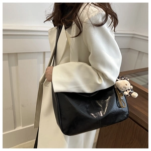 Detail of a large black glossy tote bag with a plush charm accessory on a female model