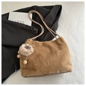 Détail d'un sac cabas marron en fausse fourrure avec charm d'ours sur tissu blanc