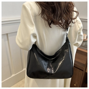Close-up of a large black glossy leather crescent bag showing stitching and texture