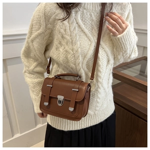 Detail of a vintage dark brown crossbody bag on a model wearing a white knit sweater
