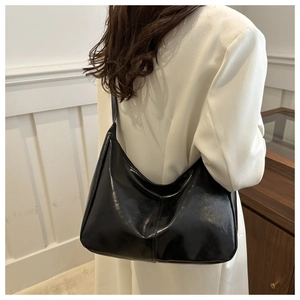 Model wearing a glossy black patent leather hobo bag showing shoulder strap fit and size