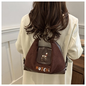 Detail of suede shoulder bag with dog embroidery and MUTEHI lettering on brown flap