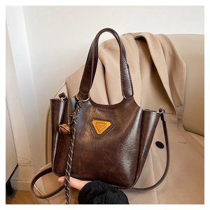 Detail of vintage brown leather bag with golden triangular logo and bell charm pendant