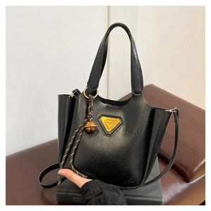 Close-up of black lychee leather tote bag featuring gold hardware and bell charm