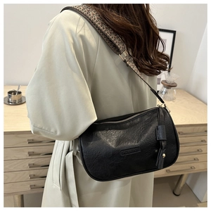 Close-up of black textured faux leather crossbody bag with wide geometric strap and logo