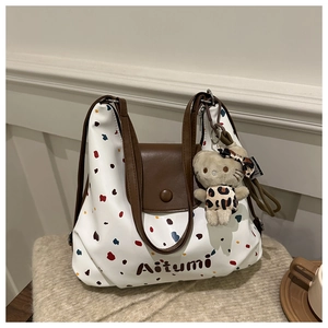Dettaglio di una borsa tote bianca a pois colorati con patta in pelle marrone e ciondolo