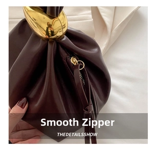 Close-up of wine red leather bucket bag featuring gold oval hardware and tassel zipper
