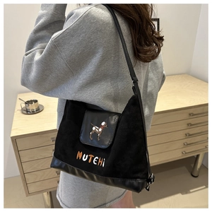 Detail of black suede tote bag with dog embroidery and MUTEHI text worn by a model