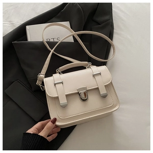 Detail of cream vintage square bag with silver metal buckles and top handle on black fabric