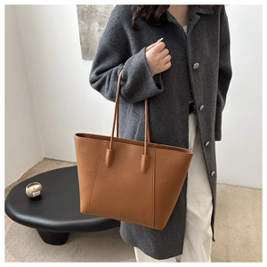 Detail of a brown lychee pattern leather tote bag with vertical stitching and reinforced handle