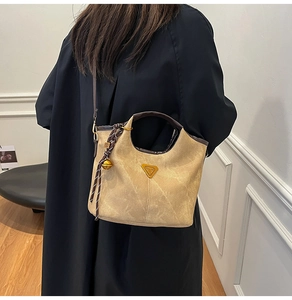 Detail of khaki bucket bag with contrast handle and woven bell charm accessory