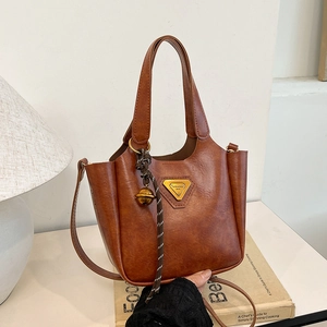 Deep brown textured faux leather tote bag with gold triangle logo and tassel on a book