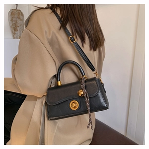 Dettaglio della borsa retrò in pelle nera con chiusura ad anello oro su un trench