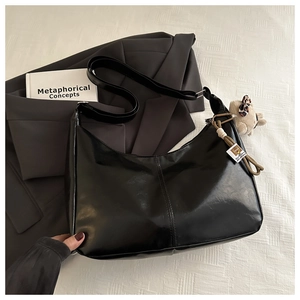 Close-up of black crescent shoulder bag with bear pendant and woven charm on a grey blazer