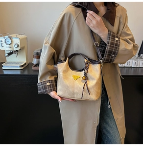Detail of vintage beige bucket bag with contrast brown handle and golden metal logo