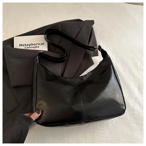 Detailed view of black polished leather hobo bag with adjustable silver buckle on a bed