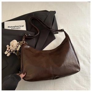 Detail of dark brown leather tote bag featuring a cute cat plush charm on the strap