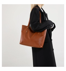 Dettaglio borsa shopper marrone con trama coccodrillo e rivetti dorati su cappotto nero