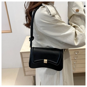 Detail of black leather bag featuring curved bottom and gold buckle on a stylish model