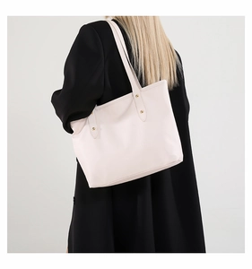 Dettaglio della borsa tote in pelle bianca con borchie dorate su cappotto nero