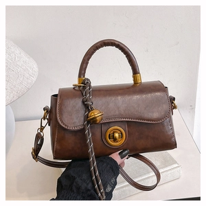 Dettaglio borsa vintage in pelle marrone con chiusura a rotazione dorata e ciondolo