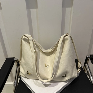 Borsa hobo bianco crema con ciondoli a farfalla dorati su una sedia nera di design