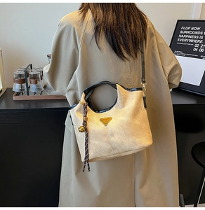 Detail of a beige canvas bucket bag with black handles and gold logo on a trench coat model