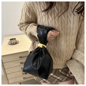 Détail d'un sac seau plissé noir avec un élégant anneau en métal doré sur la poignée