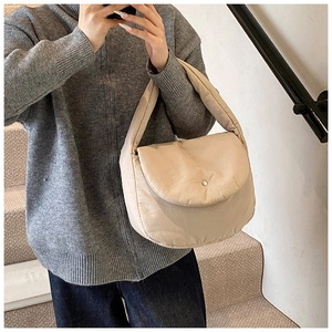 Close-up of beige quilted puffy shoulder bag with metallic snap button and soft texture