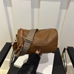 Brown cylinder shoulder bag with a wide geometric patterned strap and fashion leather tag