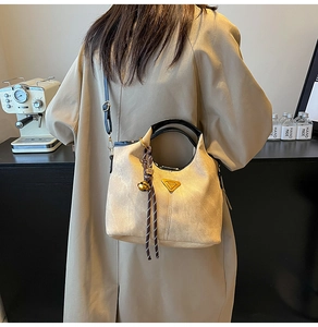 Detail of beige bucket bag with black handle, triangle metal logo and bell charm