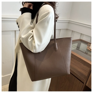 Detail of dark brown pebble leather tote bag featuring a minimalist embossed fashion logo