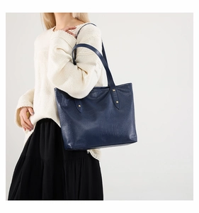 Dettaglio della borsa tote blu scuro effetto coccodrillo con finiture dorate sulla modella