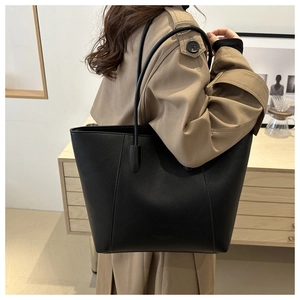 Detail of black pebbled leather tote bag with long straps shown on shoulder