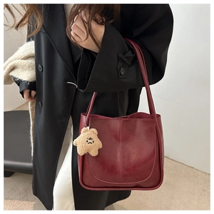 Detail of burgundy PU leather tote bag with star plush charm on a black coat outfit