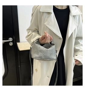 Detail of grey suede handbag with short handle and thin shoulder strap on white coat