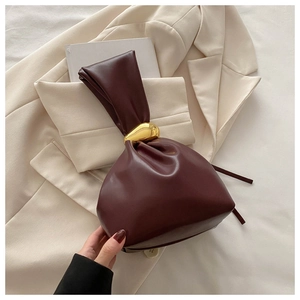 Détail du sac seau bordeaux plissé avec poignée métallique dorée sur blazer beige